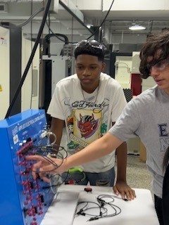 One student touching an electrical board while another student watches