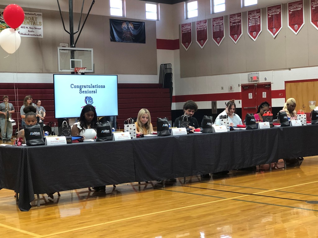 Seven student seated at long table with black tablecloth signing agreements