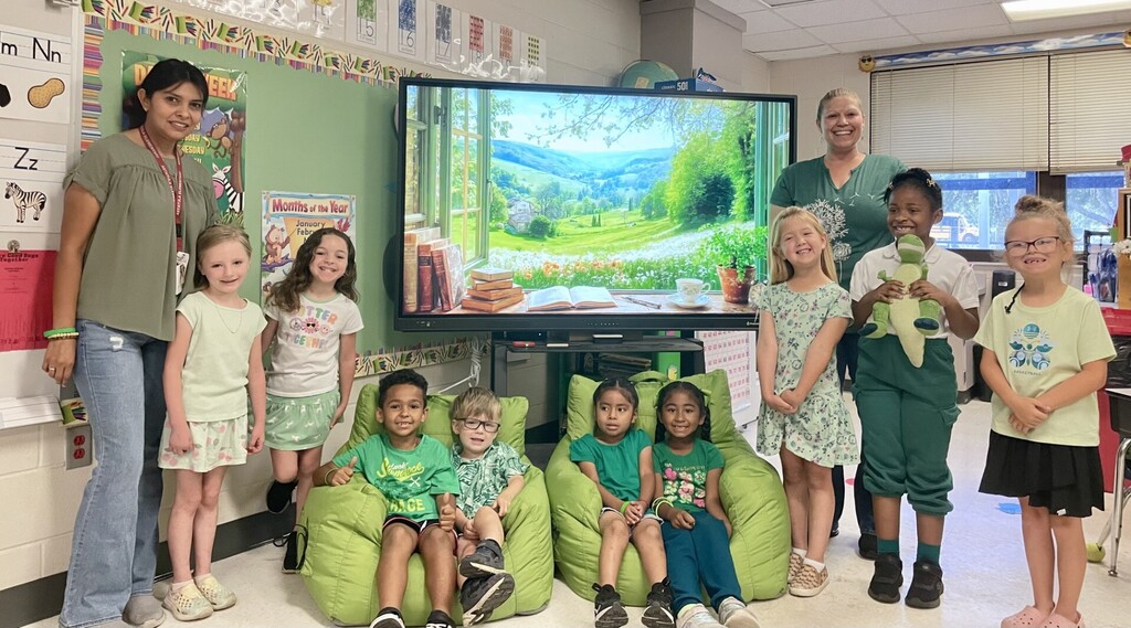 Students stand in front of a classroom promethoen board all wearing green and smiling. Celebrating Mental Health Awareness Month