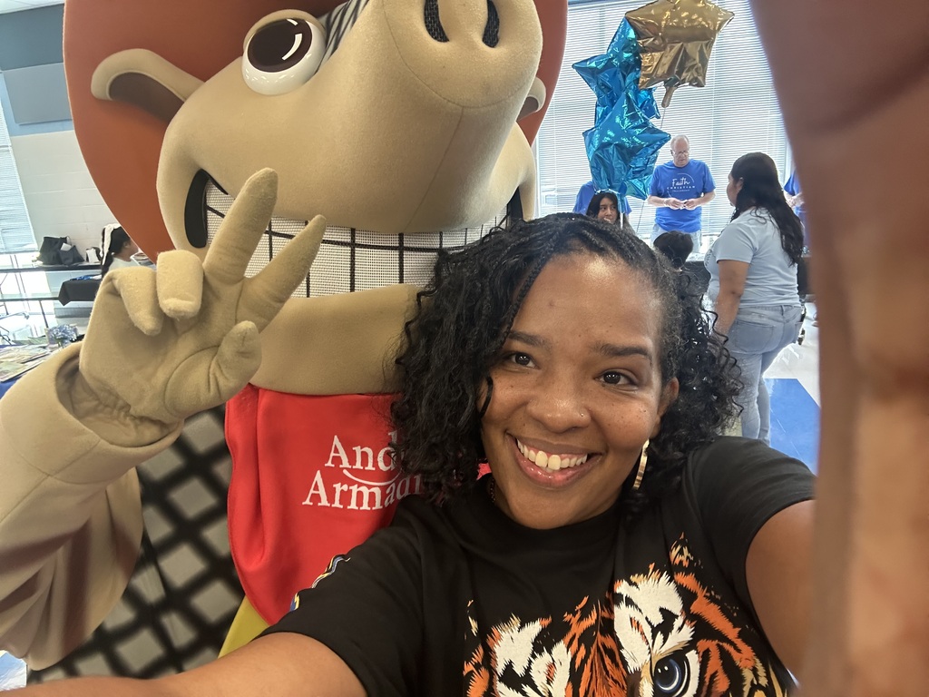 Woman smiling at a camera with a mascot wearing a red and black checkered shirt.