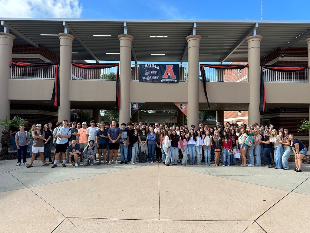 Large group of people in casual clothing pose for a photo in front of a modern building.