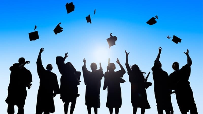 Silhouettes of people in caps and gowns stand with arms raised, tossing caps into the air.