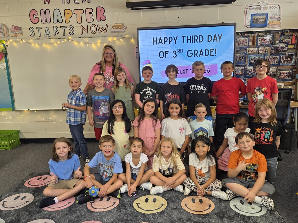 Classroom with students seated in two rows on a carpet. Behind them, a whiteboard displays a motivational message.