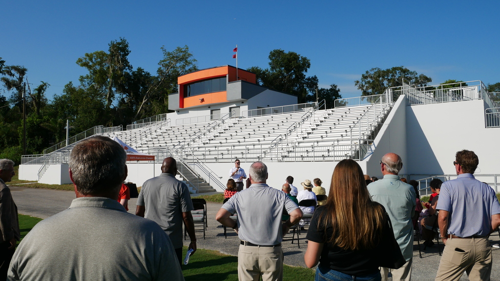 People standing facing white stadium bleachers and orange media box