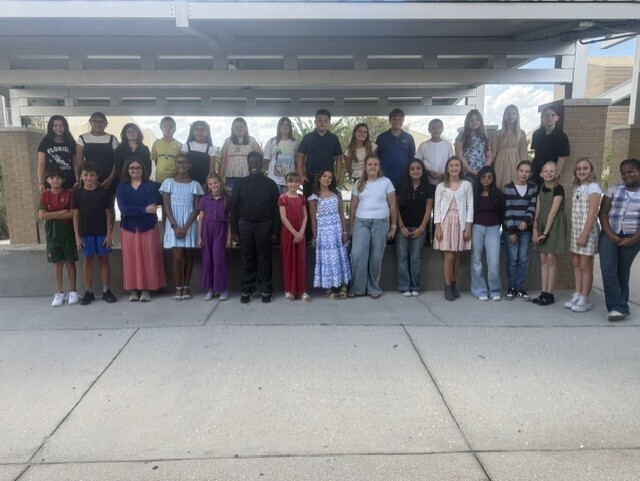 A group of students and a teacher pose for a photo under a covered walkway.