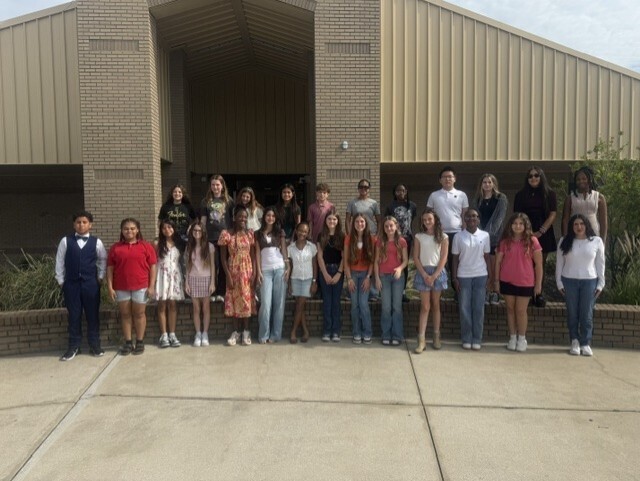 Group of students standing outside a brick building with metal panels on the sides.