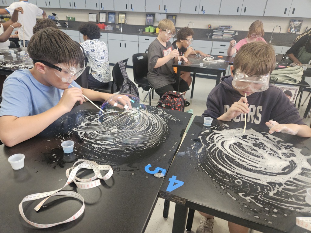 Two boys are sitting at a table, wearing goggles, and working on projects with spiral designs.