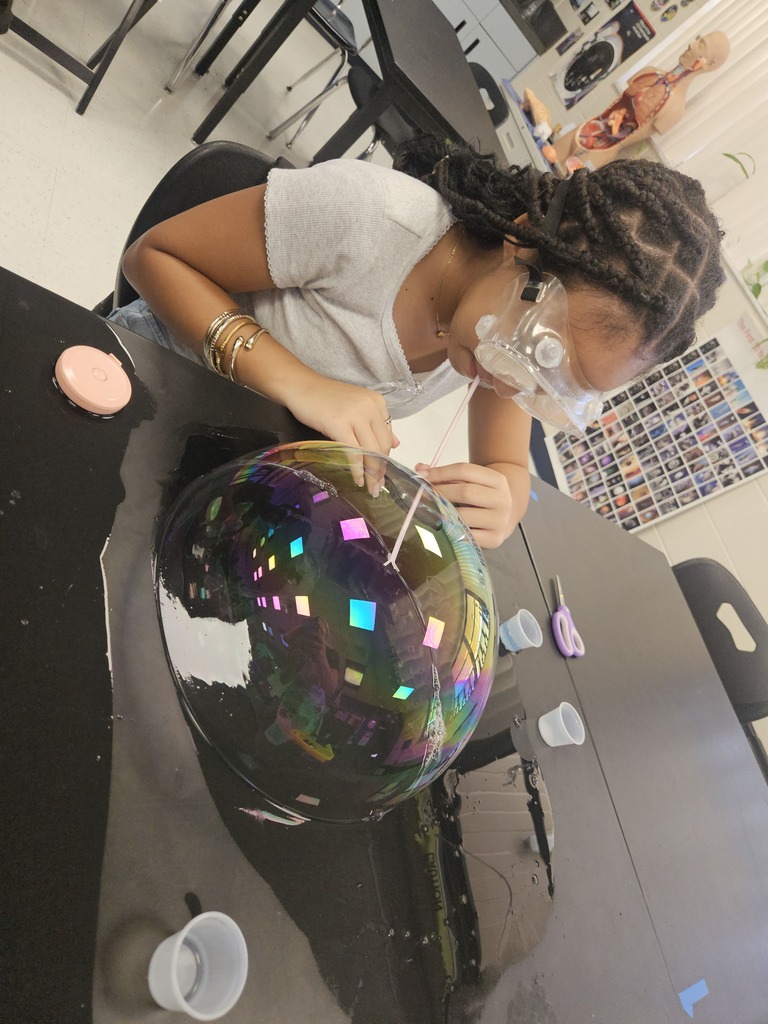 Person in a classroom setting, working with a large glass sphere with multicolored effects.