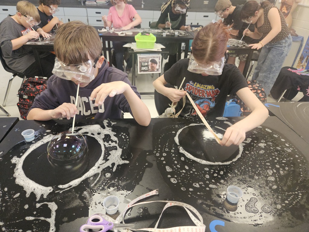 Kids in goggles and black t-shirts doing a science experiment with liquid in black bowls.