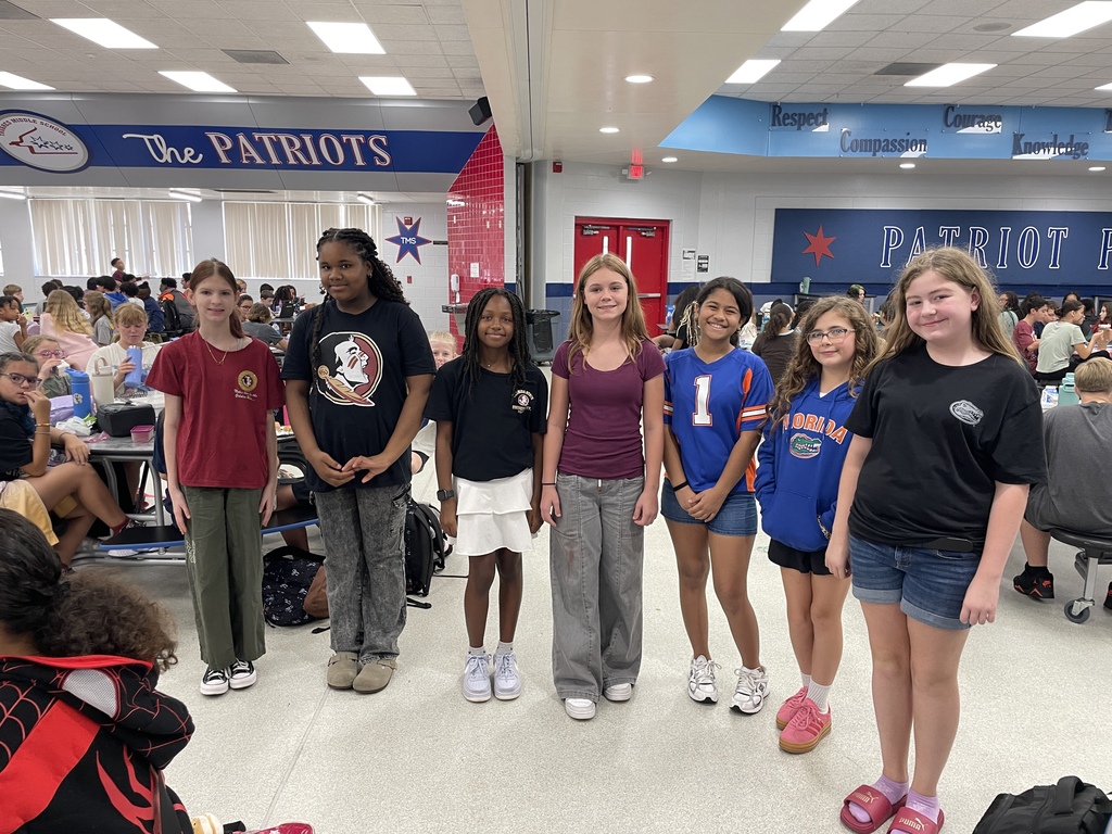 Group of students in a cafeteria, wearing matching colors, with "The Patriots" on the wall.