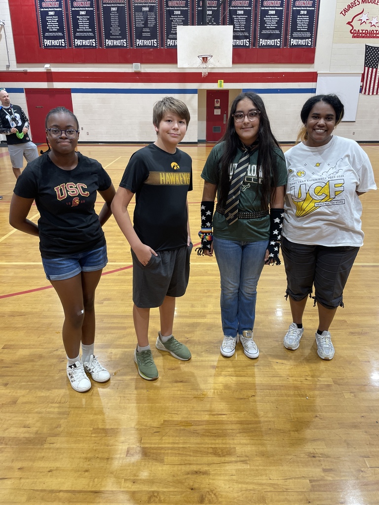 Four individuals stand together in a basketball court. Two adults and two children. One wears a wrist brace.
