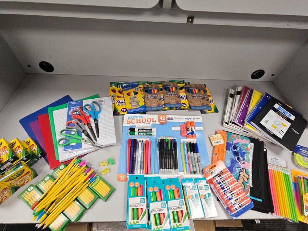 A table has assorted school supplies, including scissors, pencils, pens, markers, notebooks, and colored pencils.