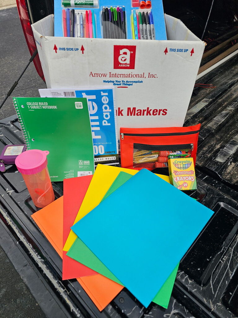 A box of colored papers, markers, notebooks, a cup, and other items on a truck bed.