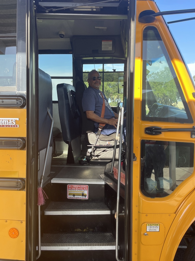 A school bus with open doors, a man in a wheelchair at the driver's seat, and a ramp inside.