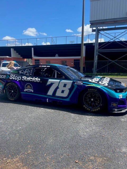 A blue and white race car with the number 78 parked on a road. A building and blue sky in the background.