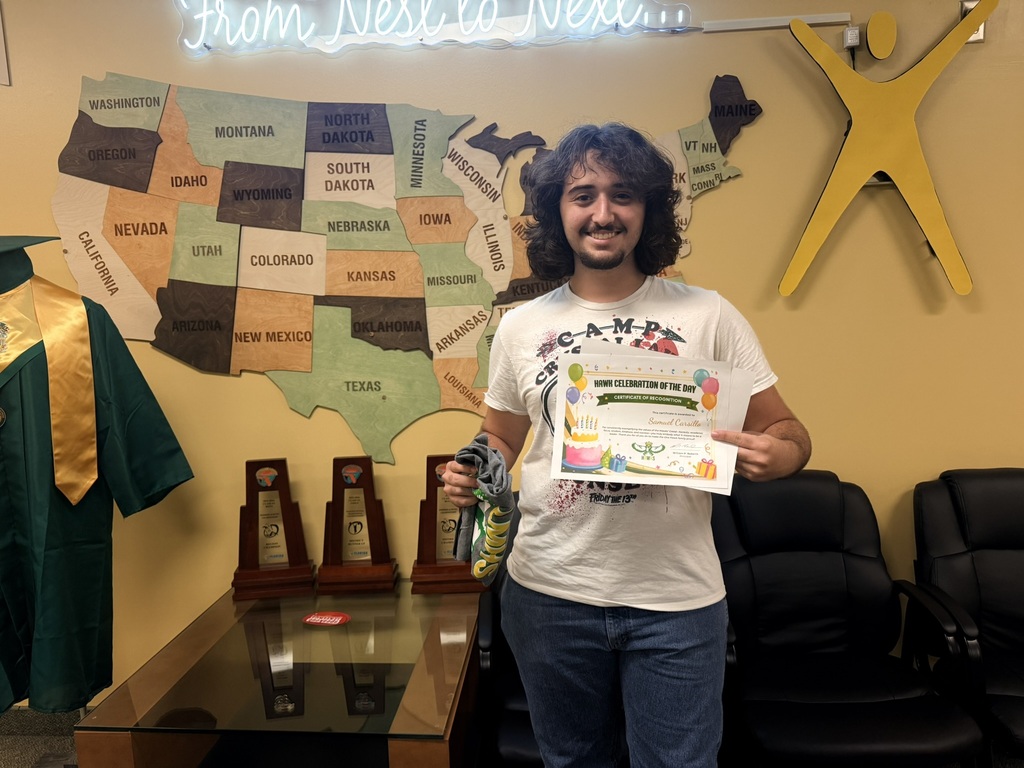 Man in white t-shirt holding certificate. He stands in room with U.S. map on wall. Black chairs in background.