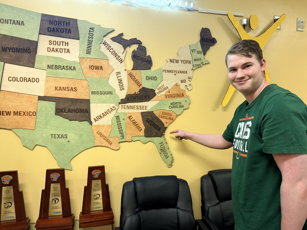 A man stands by a large map of the USA. He points to the state of Colorado.