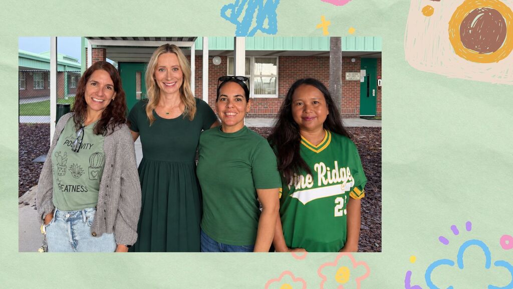 Four women stand together. One wears a green shirt with "Pine Ridge 2" on it. Background shows a building.
