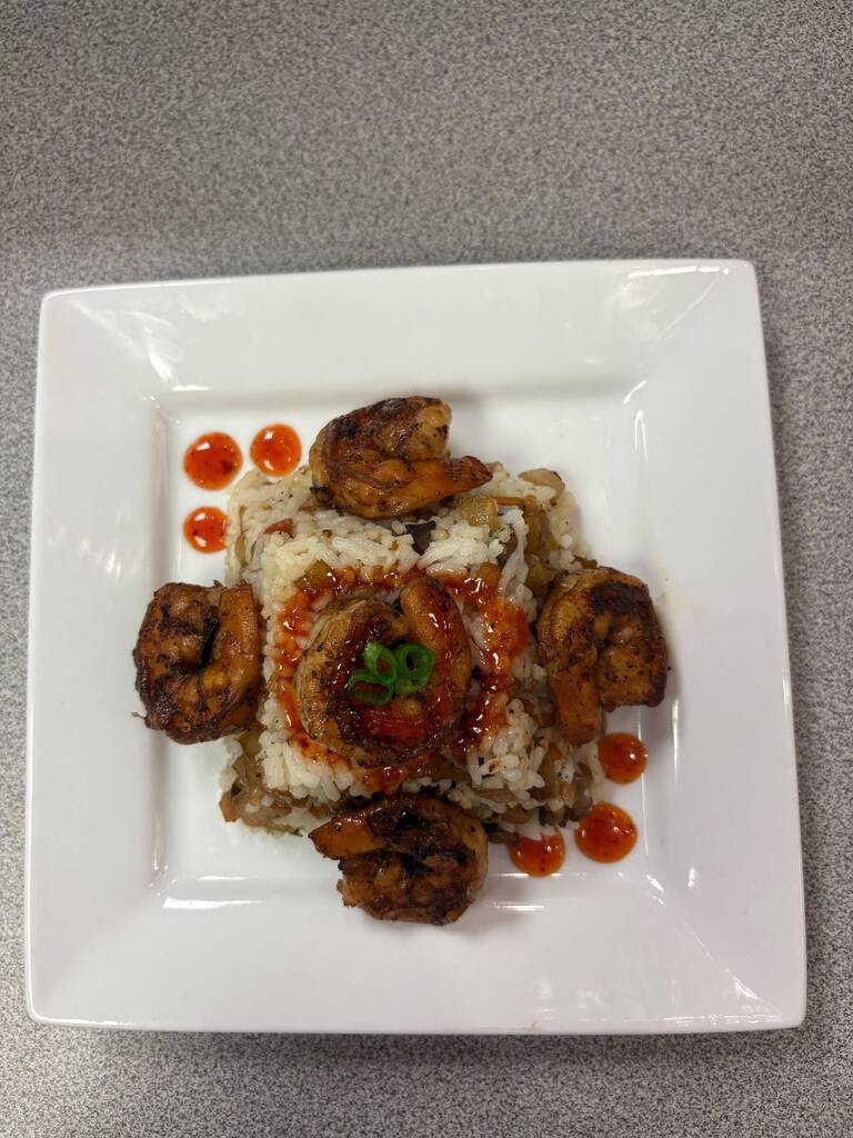 A white plate displays a dish with fried shrimp, rice, and red sauce on a gray surface.