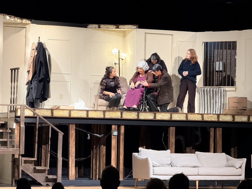 Six people on stage. One woman in a wheelchair, one woman seated on a chair. Two standing women, one man.