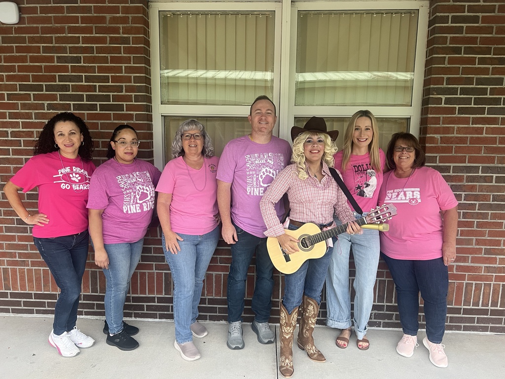 Seven people pose for a photo in pink shirts in front of a brick building.