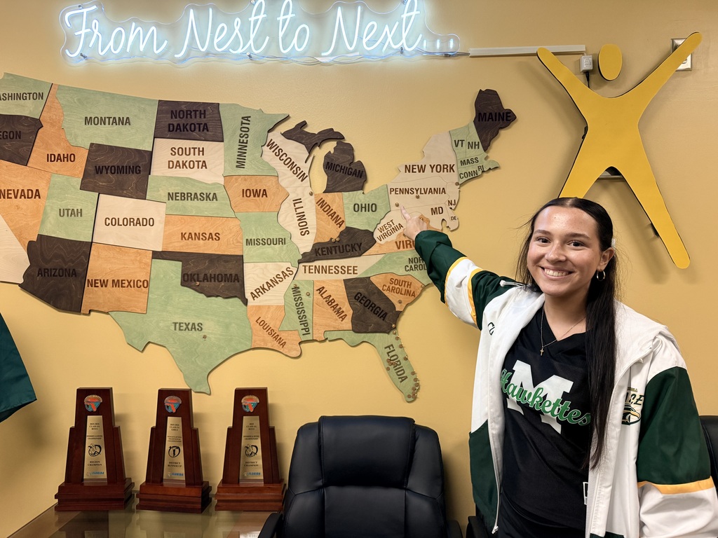 A woman stands next to a large map of the USA and three trophies on a desk.