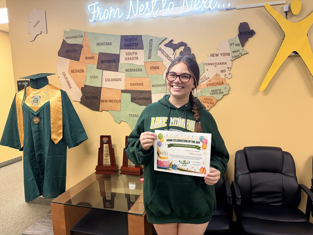 Woman holding a certificate, wearing a green sweatshirt, and standing before a map of the United States.