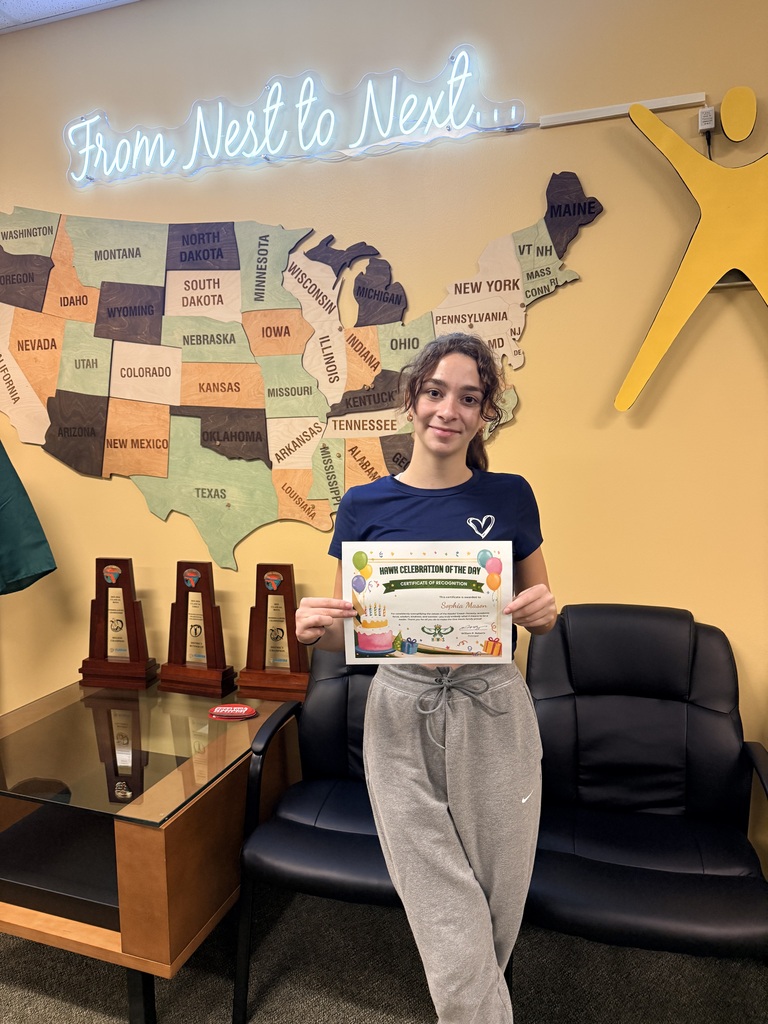 A woman holds an award certificate. She stands in front of a wall with a map and trophies.