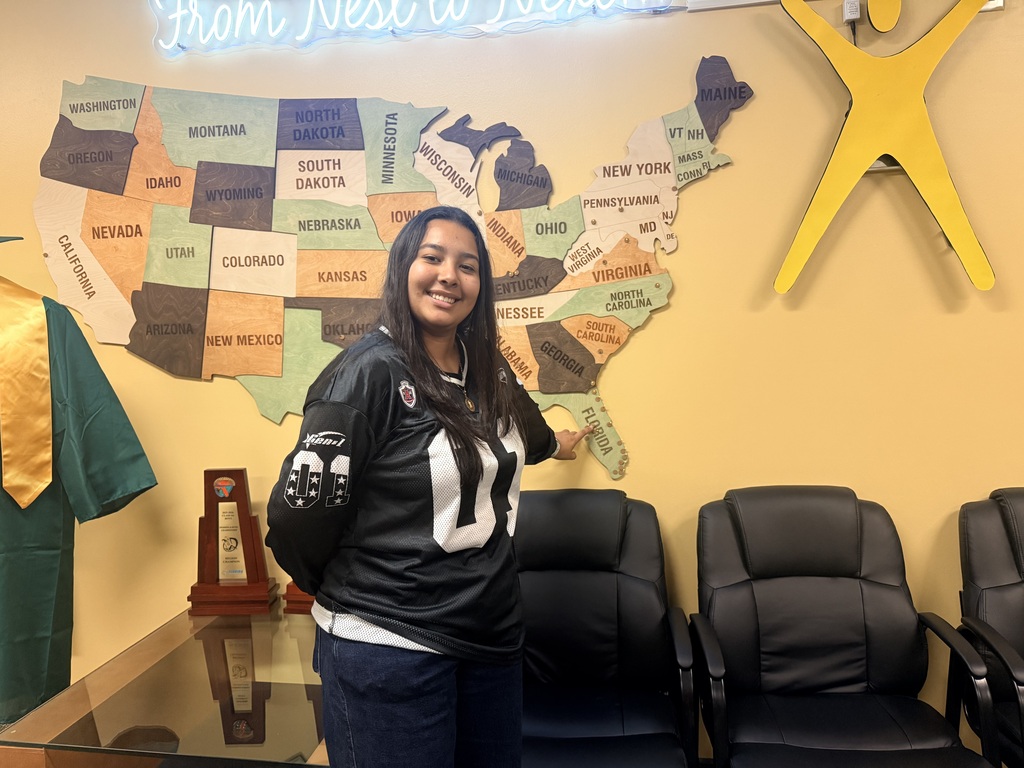 A young woman in a football jersey stands in front of a map of the US.