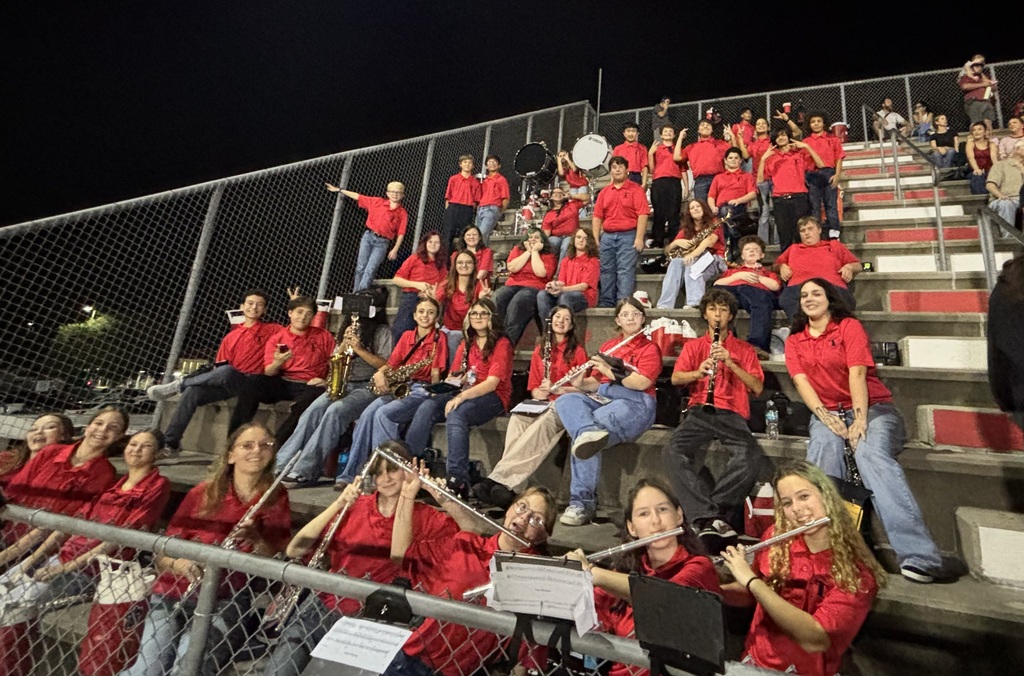 A group of people in red shirts sit on bleachers holding musical instruments, possibly during a performance.