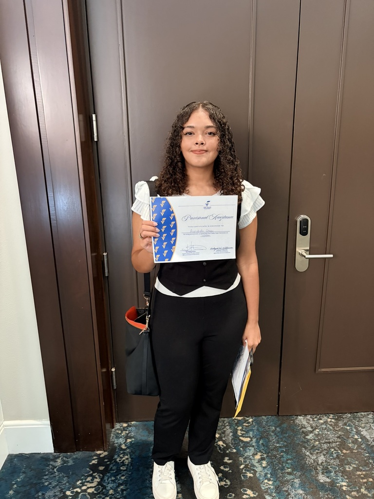 Person holding certificate, curly hair, dark pants, white top, standing by door. Blue carpet.