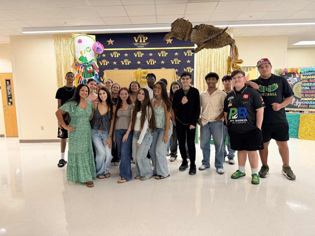 A group of people in casual clothes posing in a decorated hallway with balloons and a VIP sign.