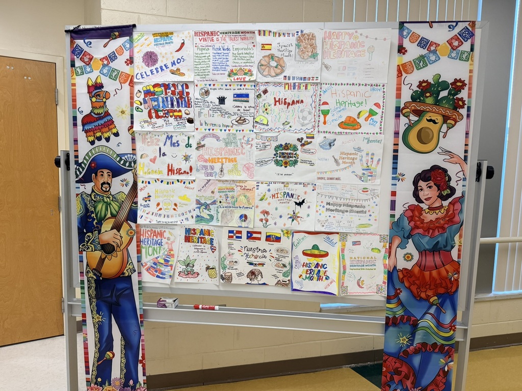 A large display board with multiple colorful illustrations, including characters in sombreros and guitars, mounted on a stand in a room.