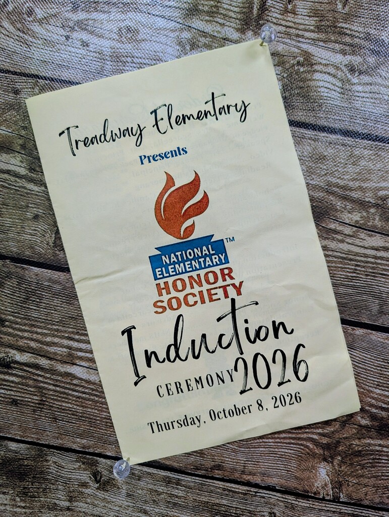 A white banner displays "National Elementary Honor Society Induction Ceremony 2026" on a wooden surface. A flame logo is above the title.