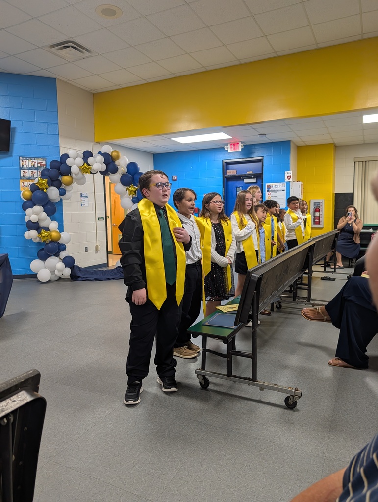 A group of young people in matching yellow and green robes standing in a room with blue and yellow walls.