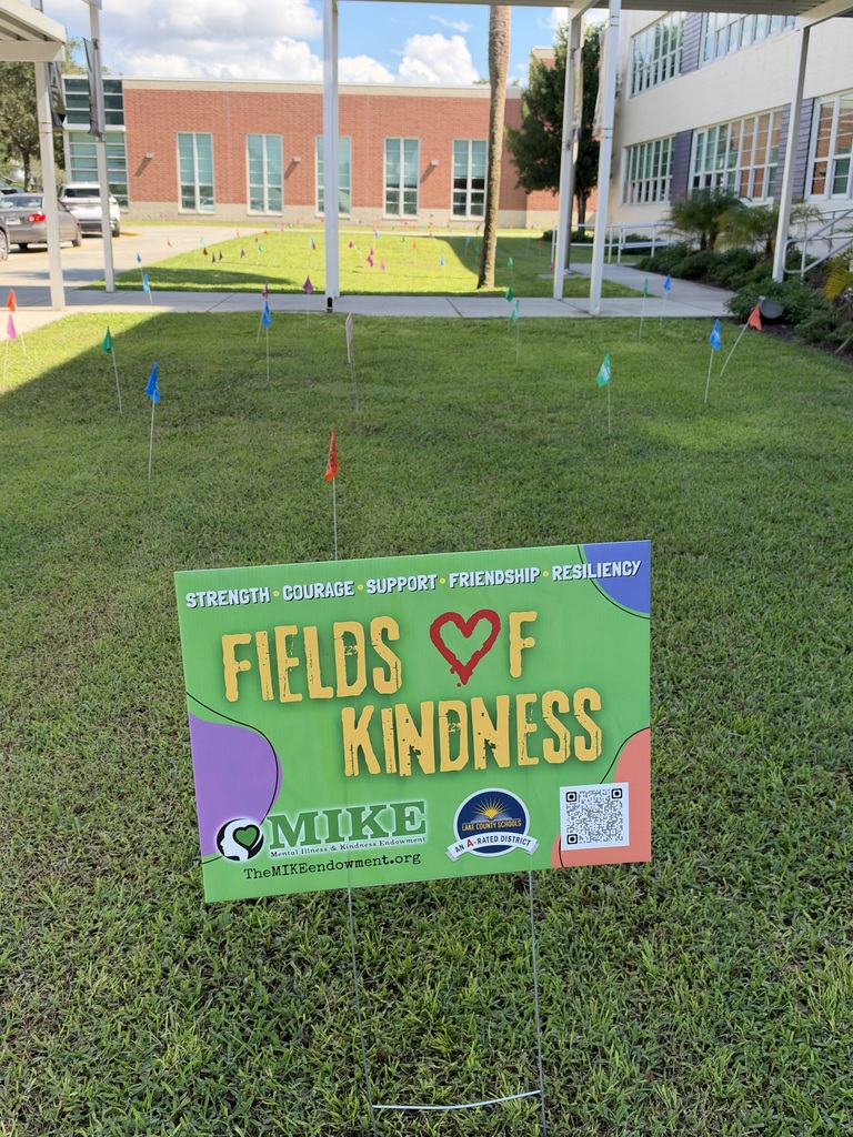 Sign on grass in front of a building. Sign reads "Fields of Kindness" with a heart and logo.