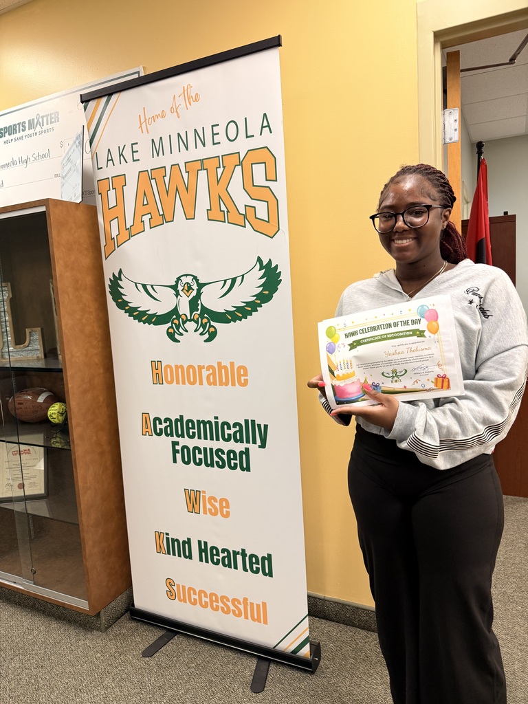 A student stands next to a school banner with an eagle and the words "Lake Minneola Hawks."