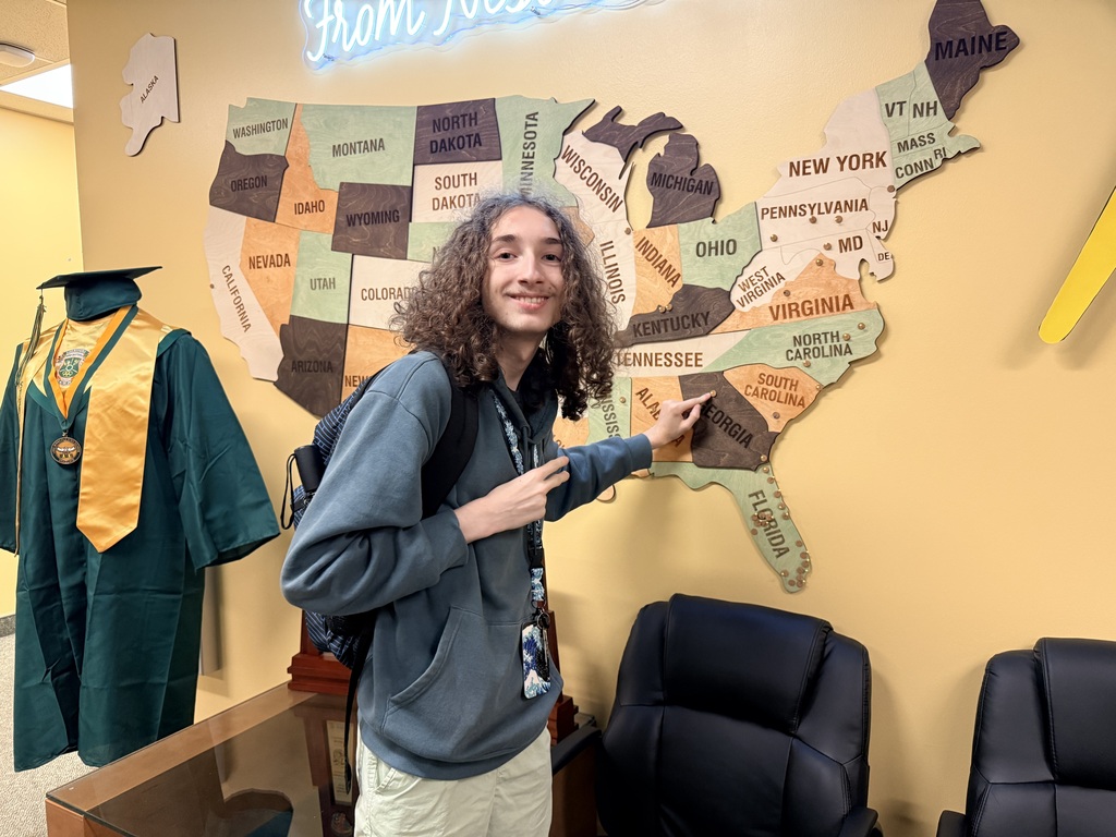 Person in a backpack stands in front of a map of the US, pointing to Virginia.