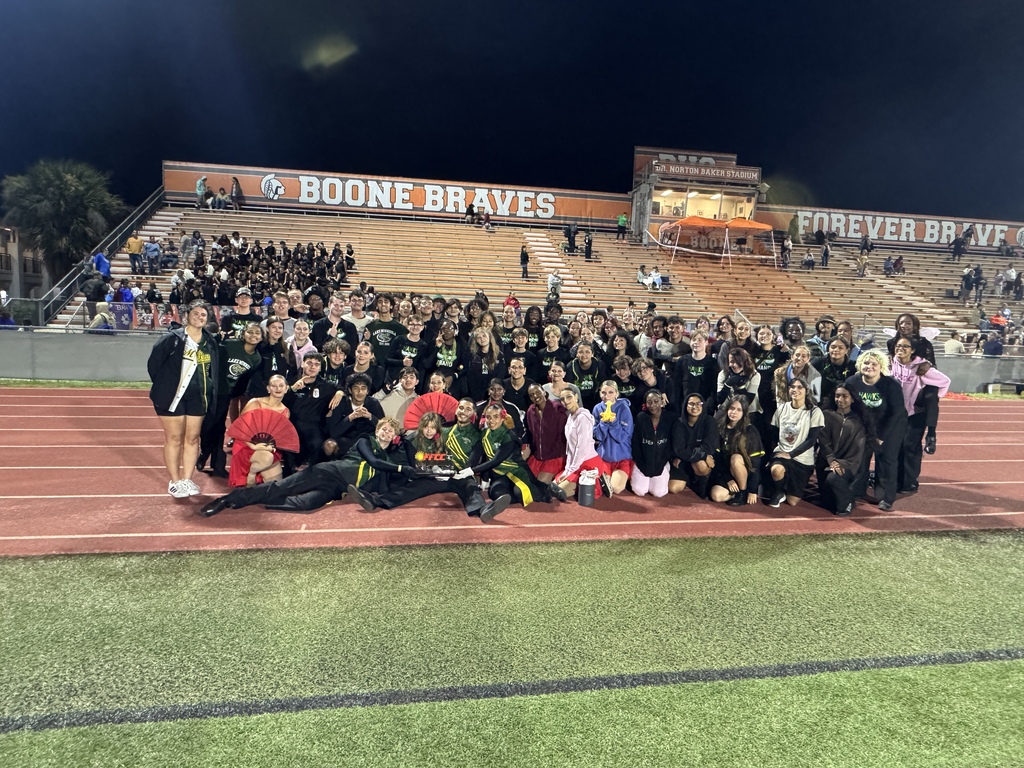 Group of people standing and sitting on a track, some in front of bleachers with "Boone Braves" sign