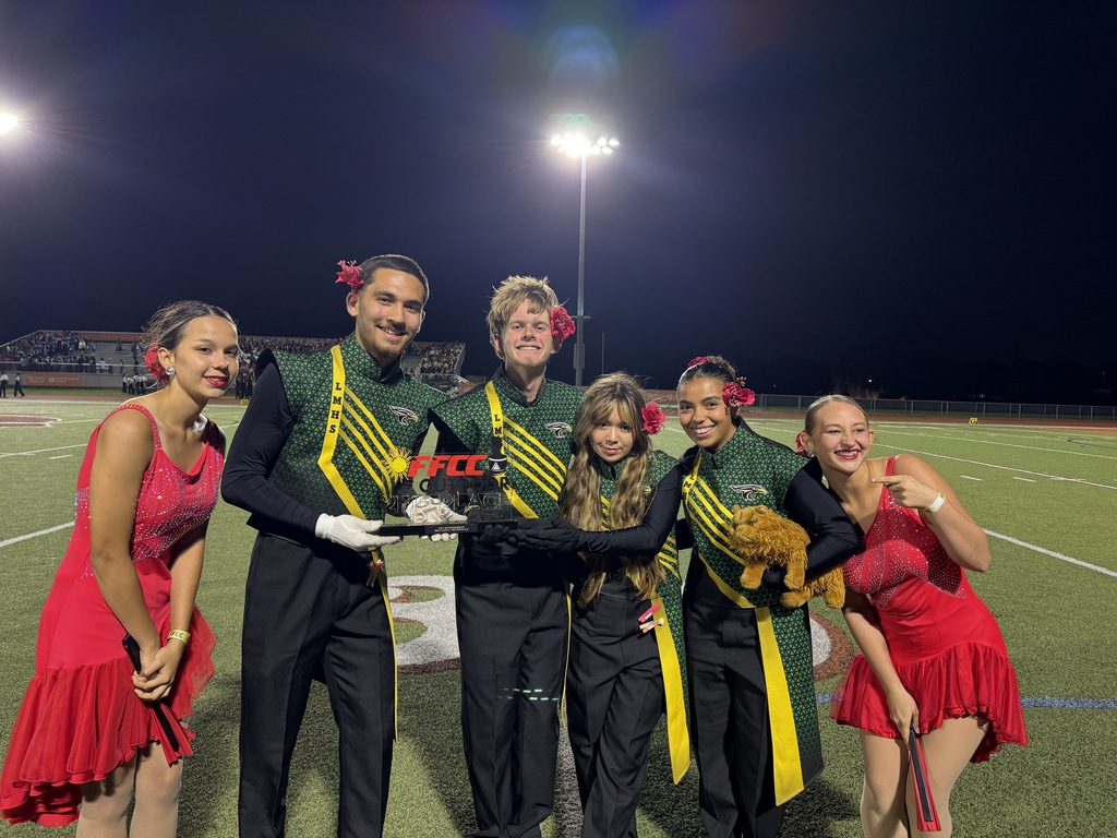 A group of young people on a football field, wearing green and yellow uniforms, posing with a trophy.