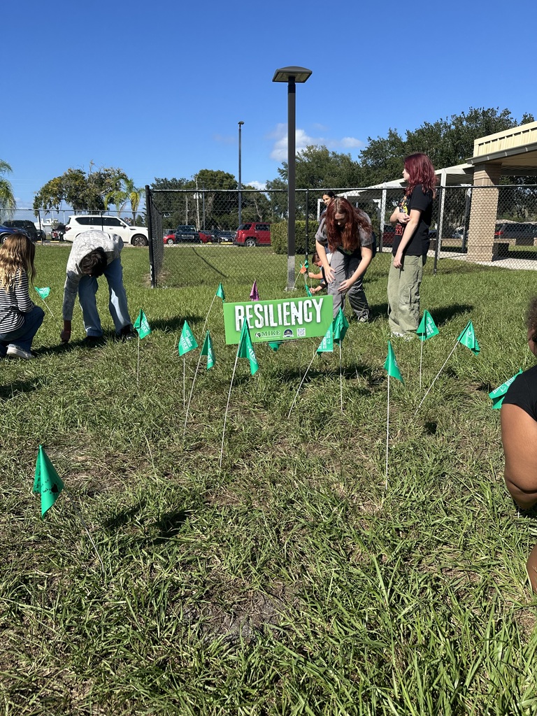 Several people are placing green flags on a grassy field with a sign that says "Resiliency."