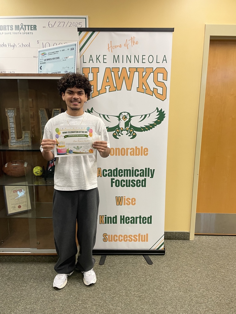 A young man holds an award in a hallway with a glass display case and a banner.