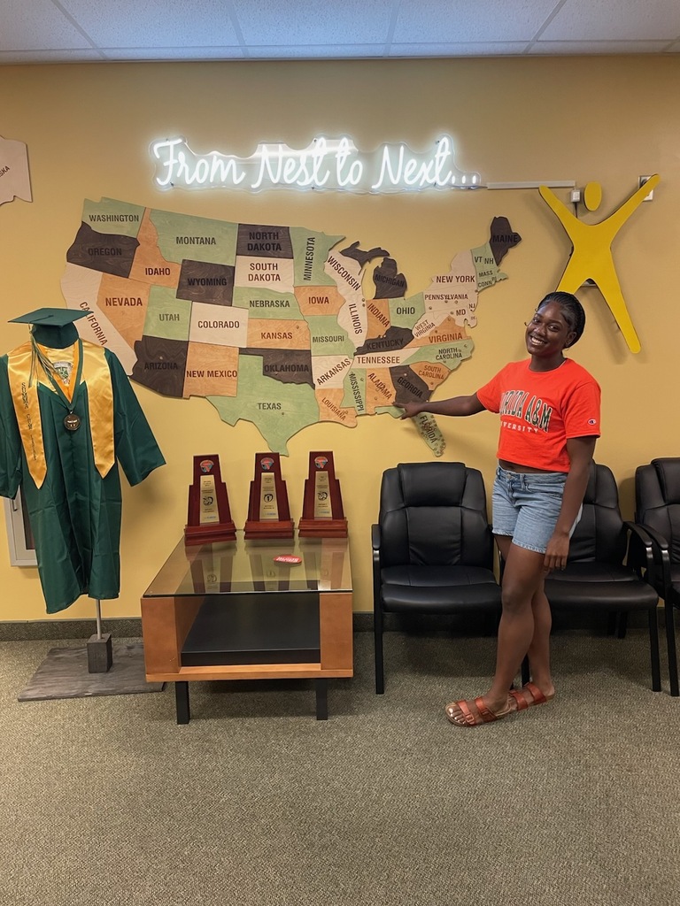 Person with cap and gown, 3 trophies, and U.S. map on wall with lighted sign.