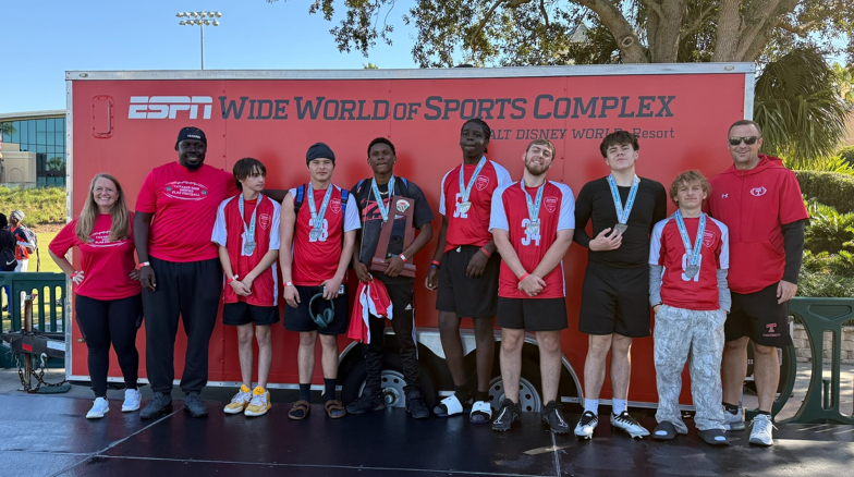 Student athletes posed and smiling. Some are wearing medals. One is holding a trophy. Wording in background says, "ESPN Wide World of Sports Complex, Walt Disney World Resort"