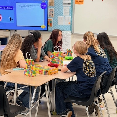 6 students sit at table with colorful bags and instructions