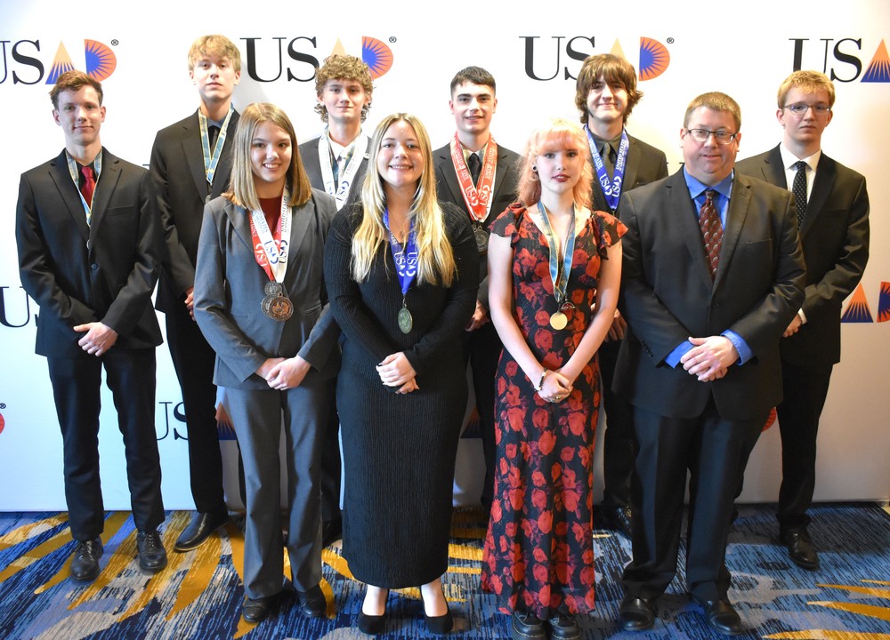students standing in front a background that says USAD, looking at the camera and smiling.