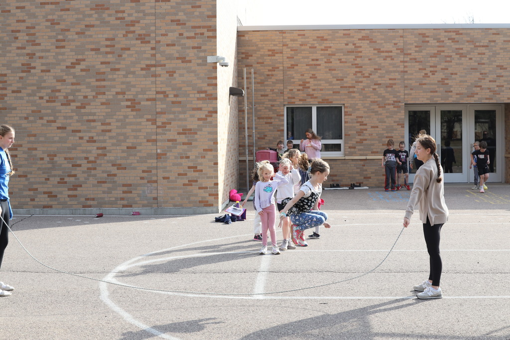 Little girl jumping over long jump rode being spun by older girls.