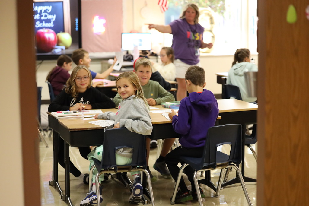 Kids smiling at camera from their desk/classroom. 