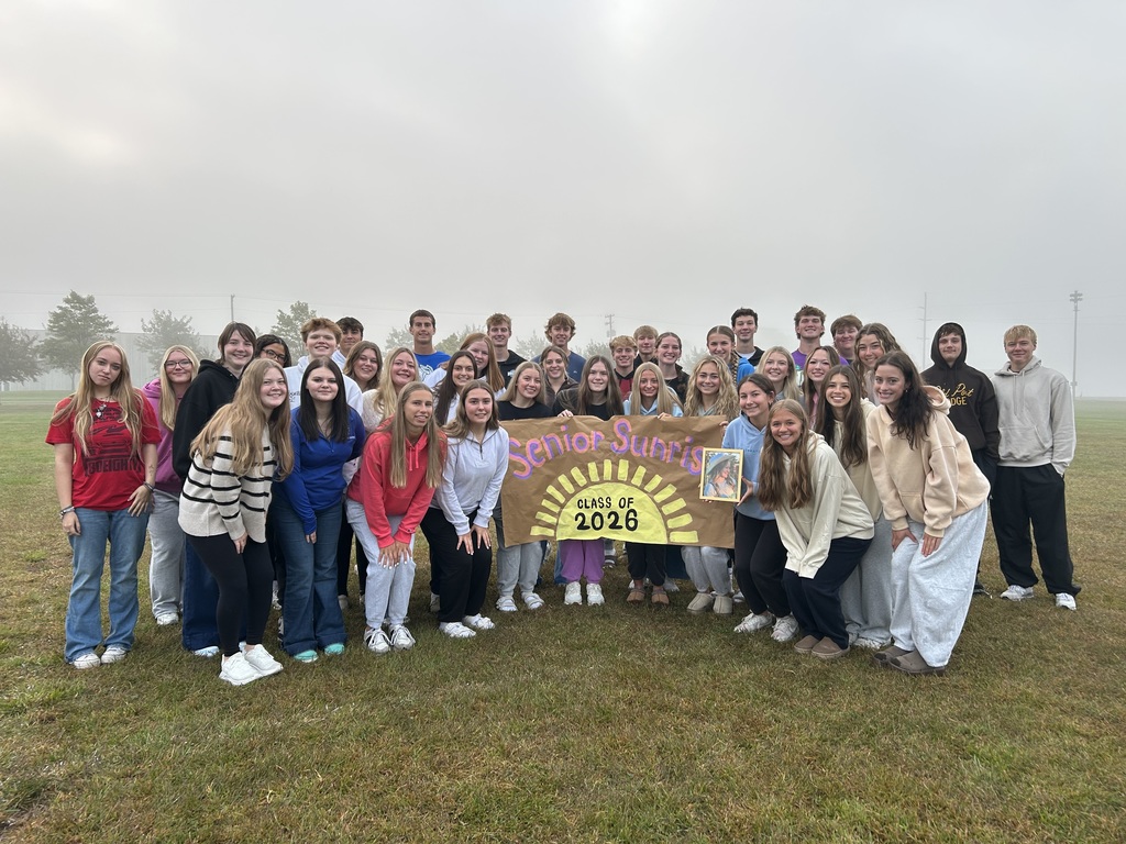 Seniors posing for the camera holding a senior sunrise banner in front of cloudy/foggy skies.