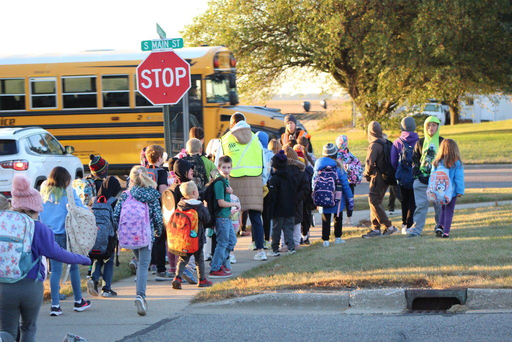 Students and staff walking to school with a bus in the background.